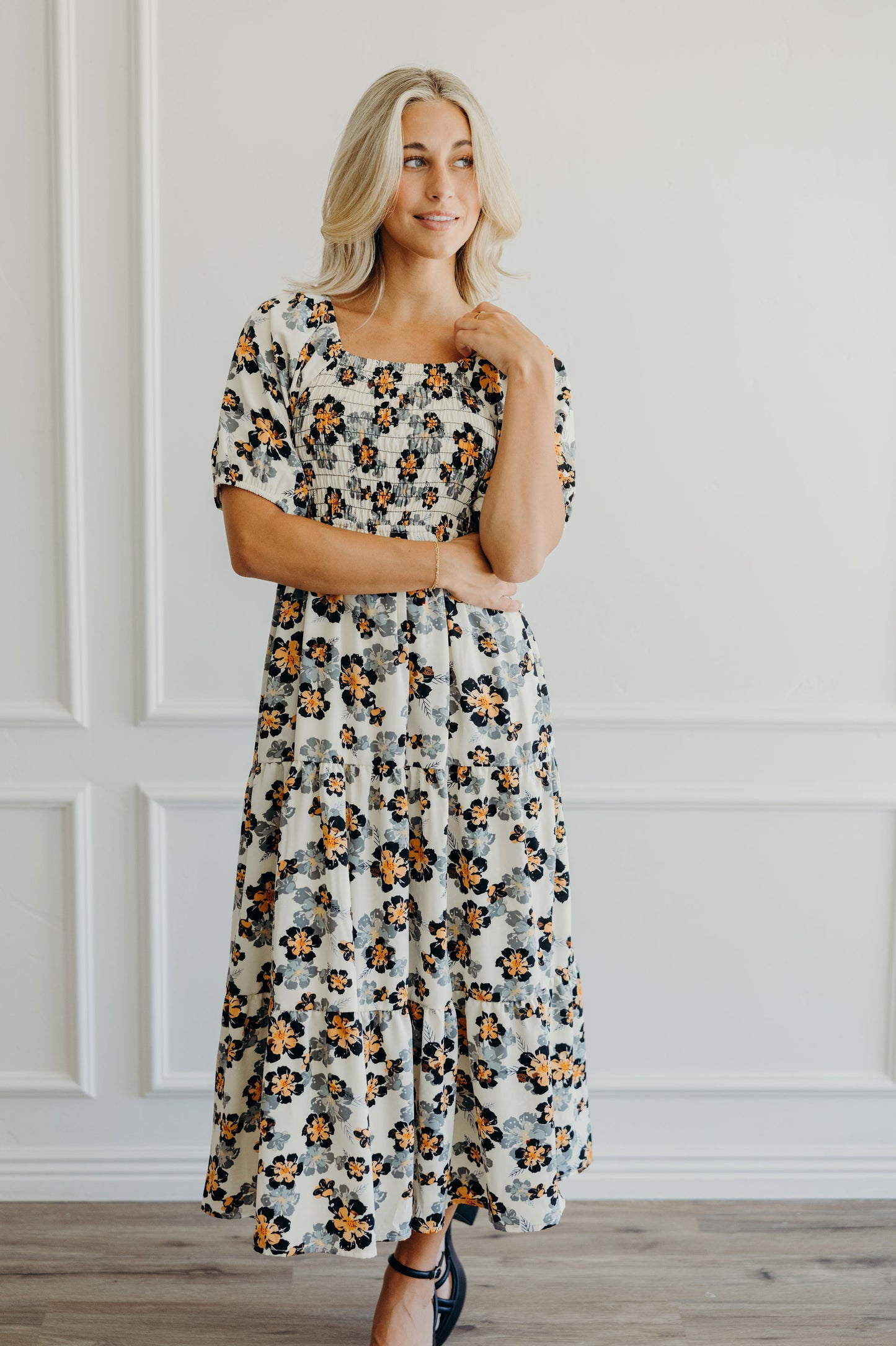 Fit and flare cream dress with black and orange floral print, smocked bodice, tiered skirt, and half sleeves.