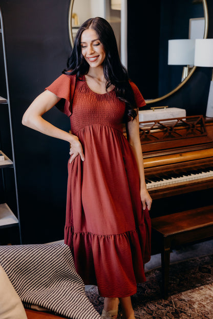 Dark red dress with smocked bodice, v neckline, flutter sleeves, and ruffle hem.